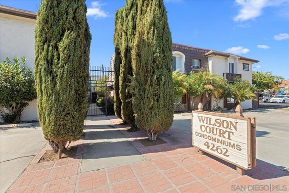 Front view of a condominium building with a gated entrance and a sign reading 'Wilson Court Condominiums 4262.'