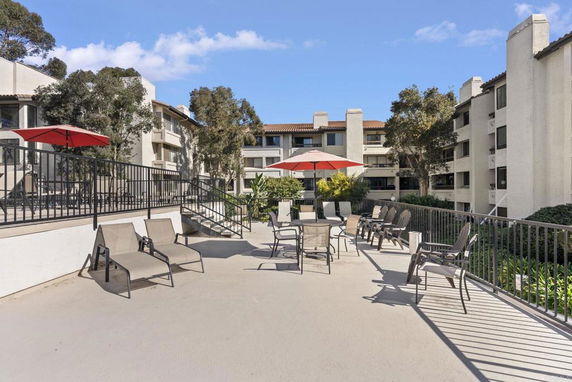 Rooftop patio area with lounge chairs and umbrellas on a multi-story building.