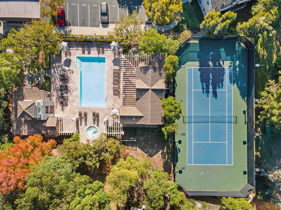 Aerial view of a swimming pool and tennis court surrounded by trees.