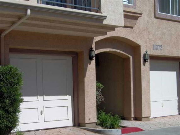 Front view of a house with an arched entryway and white garage doors.