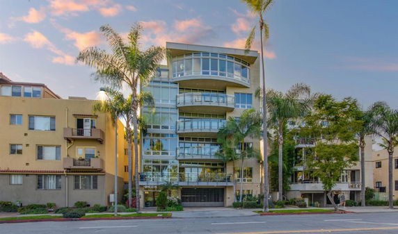 Front view of a multi-story building with glass balconies and palm trees in front.