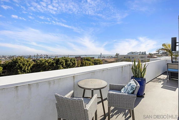 Rooftop seating area with a table and chairs, offering a panoramic view of the cityscape and distant water body.