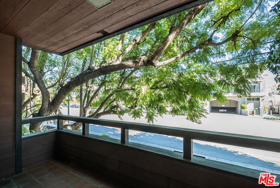 View from a balcony overlooking a street with trees and buildings.