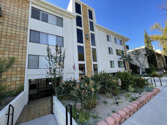 Front view of a multi-story building with large windows and landscaped entrance.