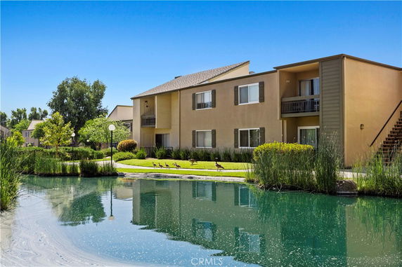 Front view of a two-story apartment building with a pond in the foreground.