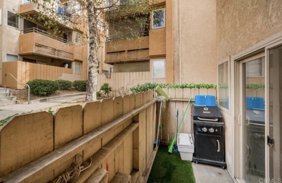 Outdoor view of apartment balconies with a fenced area containing a grill and cleaning tools.