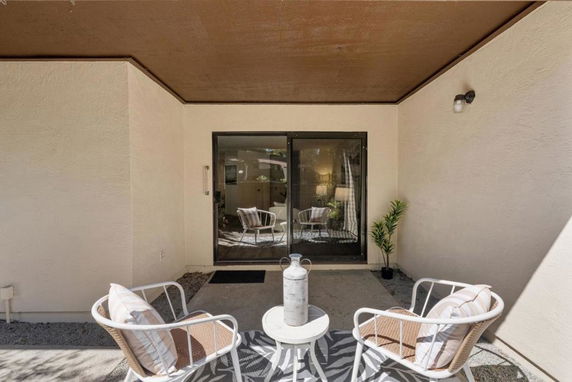 Front view of a small patio area with two chairs and a table in front of a sliding glass door.