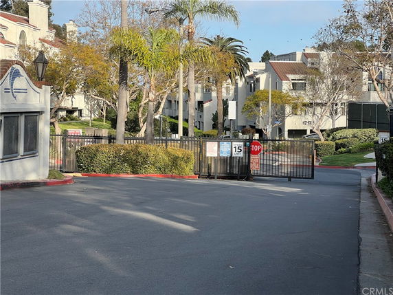 View of an apartment complex entrance with a security gate and multiple buildings in the background.