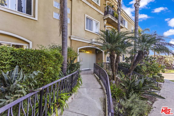 Front view of a multi-story building with a walkway and lush landscaping.