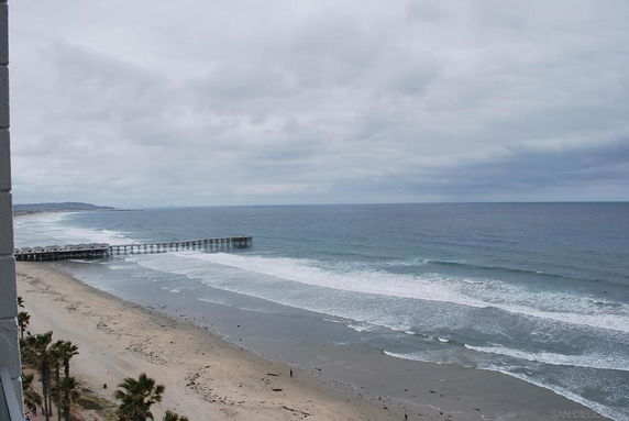 Wide view of a sandy beach with ocean waves and a pier extending into the water.