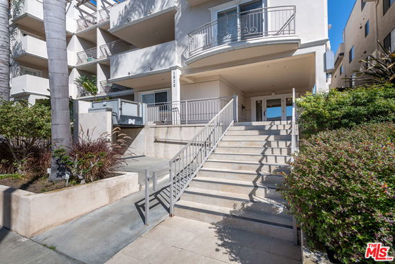 Front view of a multi-story residential building with balconies and stairs leading to the entrance.