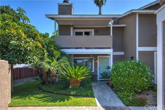 Front view of a two-story house with a small balcony and surrounding greenery.