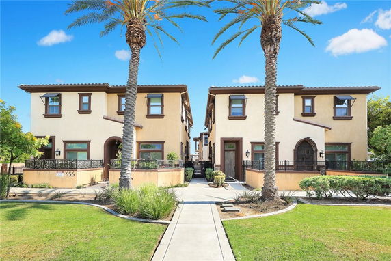 Front view of a two-story house with two symmetrical units and a central walkway, featuring palm trees in front.