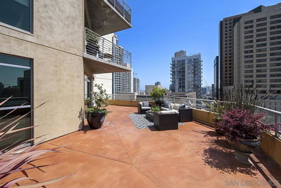 Rooftop terrace with outdoor seating and potted plants, overlooking city buildings.