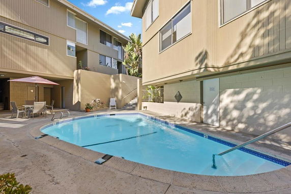 View of an outdoor swimming pool surrounded by a multi-level building with seating area and umbrella.
