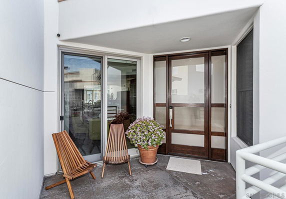 Outdoor entryway of a building with a glass door and two wooden chairs.