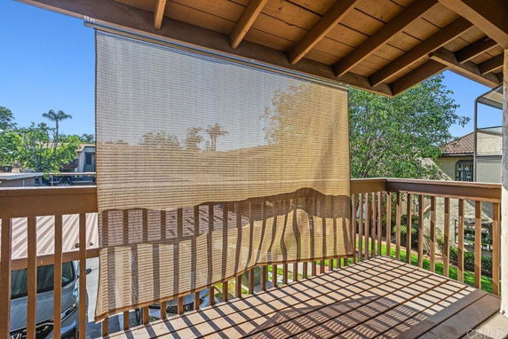 View from a wooden balcony with a sunshade looking out towards trees and neighboring buildings.
