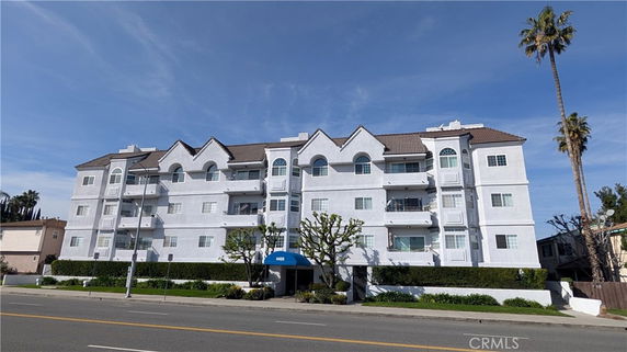 Front view of a multi-story apartment building with balconies and a tiled roof.