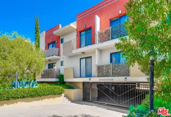 Front view of a multi-story apartment building with balconies and gated parking.