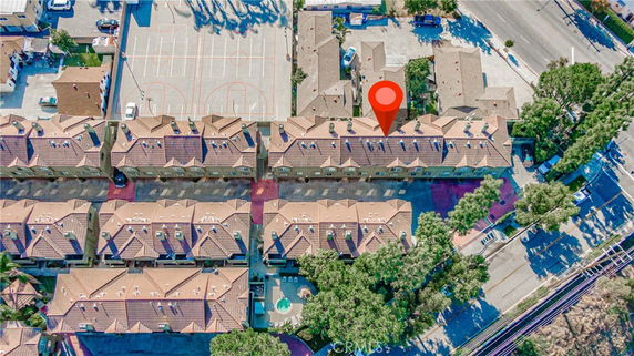 Aerial view of a residential complex with several rows of connected townhouses and a basketball court, surrounded by roads and trees.