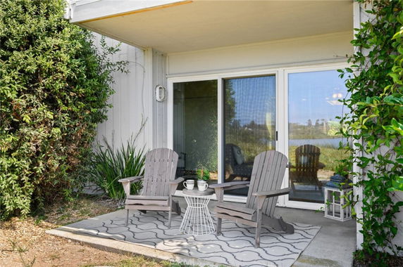 Patio area with chairs and a small table in front of a sliding glass door, overlooking greenery and water.