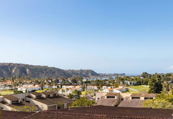 Panoramic view of a coastal area with residential buildings and hills in the background.