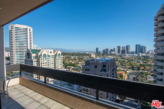 Panoramic cityscape view from a high-rise balcony overlooking multiple buildings.