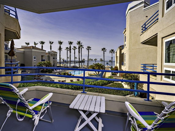 Balcony view overlooking a pool area with buildings and palm trees in the background.
