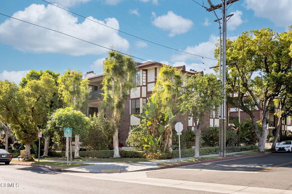 Front view of a multi-story apartment building with balconies and surrounded by trees.