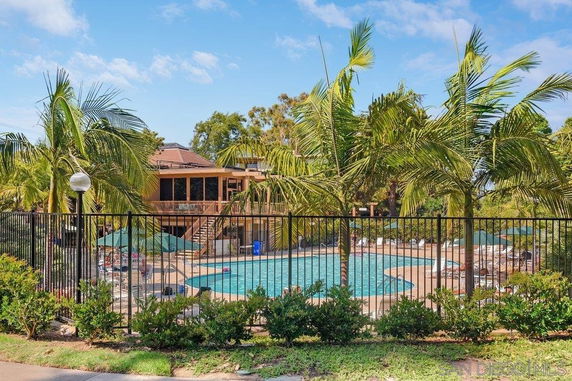 Outdoor view of a swimming pool area with umbrellas and lounge chairs surrounded by palm trees.