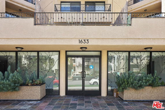 Front entrance of a multi-story building with decorative glass panels and planters.
