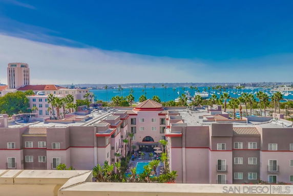 Aerial view of a coastal apartment complex with multiple buildings and a waterfront marina in the background.