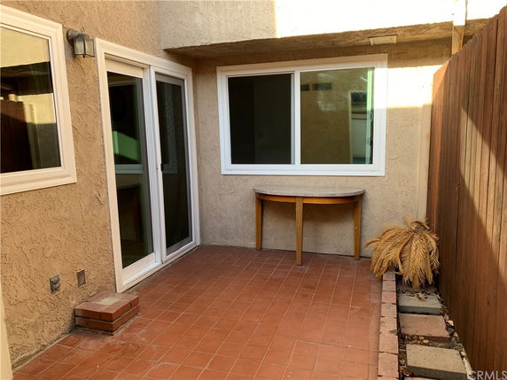 Small outdoor patio area with tiled floor, surrounded by a wooden fence and walls with sliding glass doors.