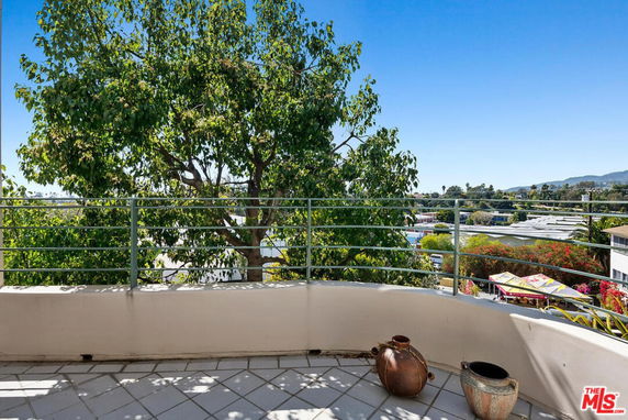 Balcony view with railing overlooking greenery and distant buildings.