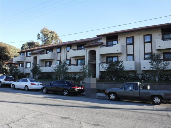Front view of a multi-story residential building with balconies and a parking area in front.