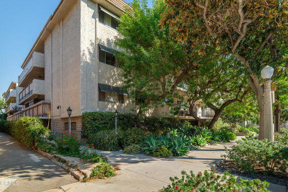 Front view of a multi-story apartment building with balconies and surrounding trees.