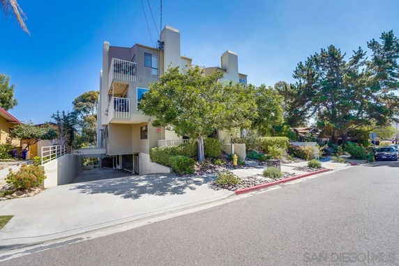 Front view of a multi-story residential building with balconies and a driveway leading to parking underneath.