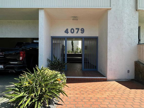 Front view of a house entrance with a partially visible parking area.