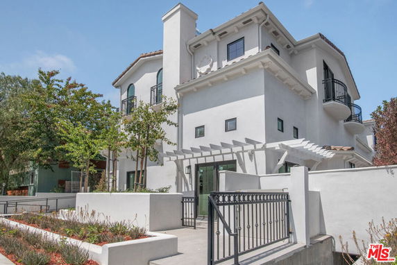 Front view of a multi-story white house with balconies and a pergola.