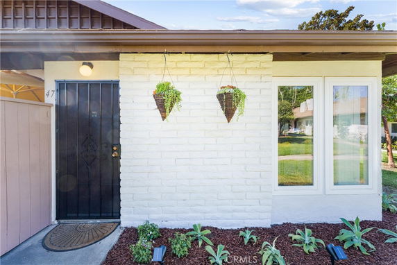 Front view of a house with a black door, white brick wall, and hanging plants.