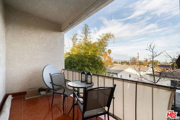 Outdoor patio area with a small table and chairs overlooking residential rooftops and trees.