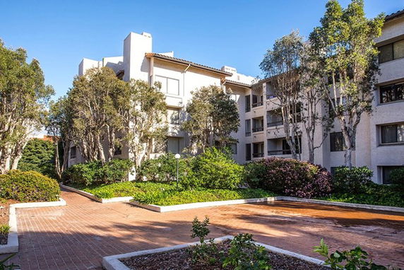 View of a residential building with surrounding greenery and paved walkways.