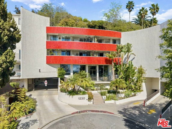 Front view of a multi-story building with a red accent and greenery at the entrance.