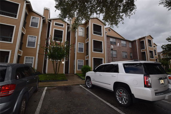 Front view of a multi-story building with wooden siding and brick, featuring balconies and multiple windows.