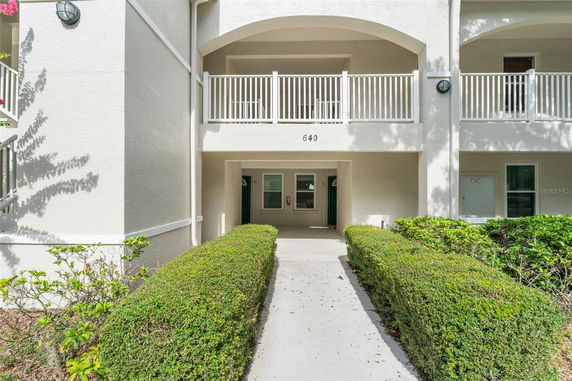 Front view of a building with an archway and balcony, leading to an entrance walkway.