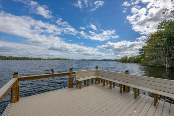 Wide-angle view of a wooden deck overlooking a large body of water with trees in the background.