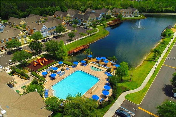 Aerial view of a residential area with a swimming pool, outdoor play area, and a lake with a fountain.