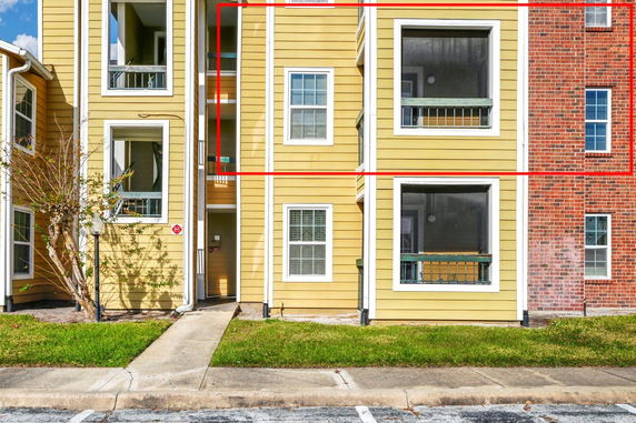 Front view of a multi-story apartment building with yellow siding and large windows.