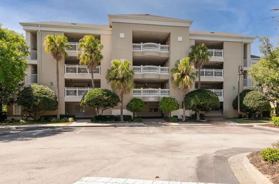 Front view of a multi-story building with white balconies and surrounding trees.
