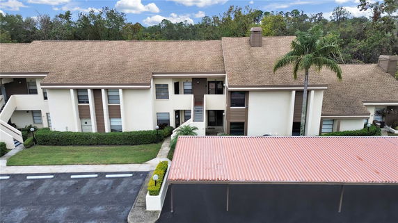 Front view of a multi-story residential building with a brown roof and white facade, featuring a central staircase and a nearby palm tree.